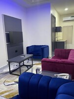 Una sala de estar moderna con un televisor de pantalla plana montado en la pared, un sofá azul, un sofá rojo y una pequeña mesa con un control remoto.