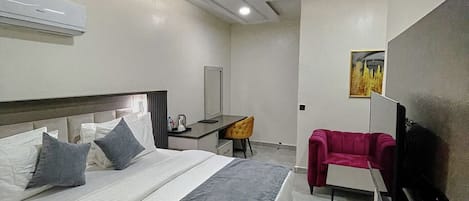 A modern hotel room with a large bed, a desk, a chair, and a TV.