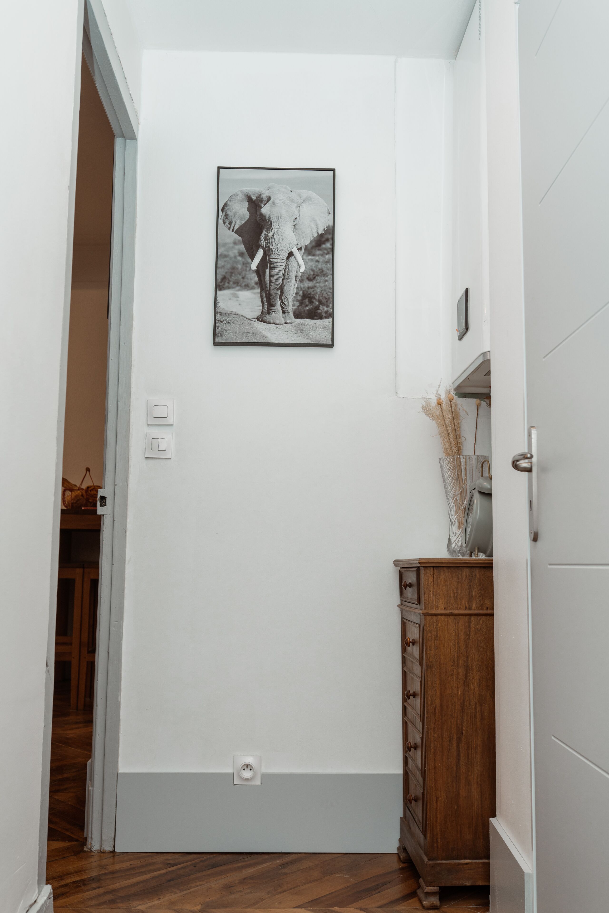 A hallway with a wooden cabinet, a framed picture on the wall, and a door leading to another room.