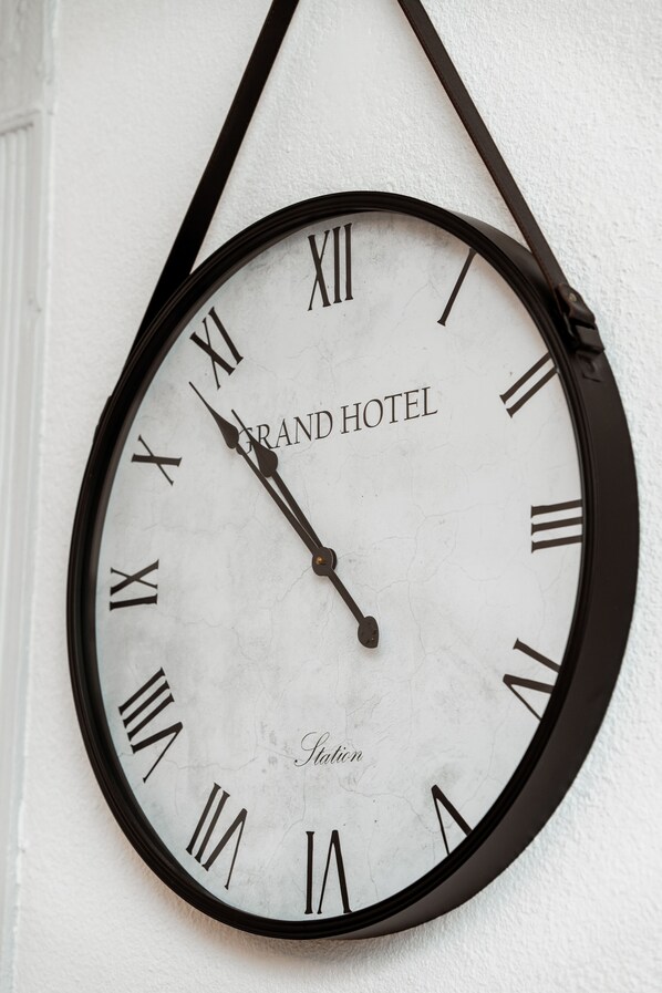 Seinään kiinnitetty kello, jossa on roomalaiset numerot sekä sanat »GRAND HOTEL» ja »Station» maalattuna sen pintaan.