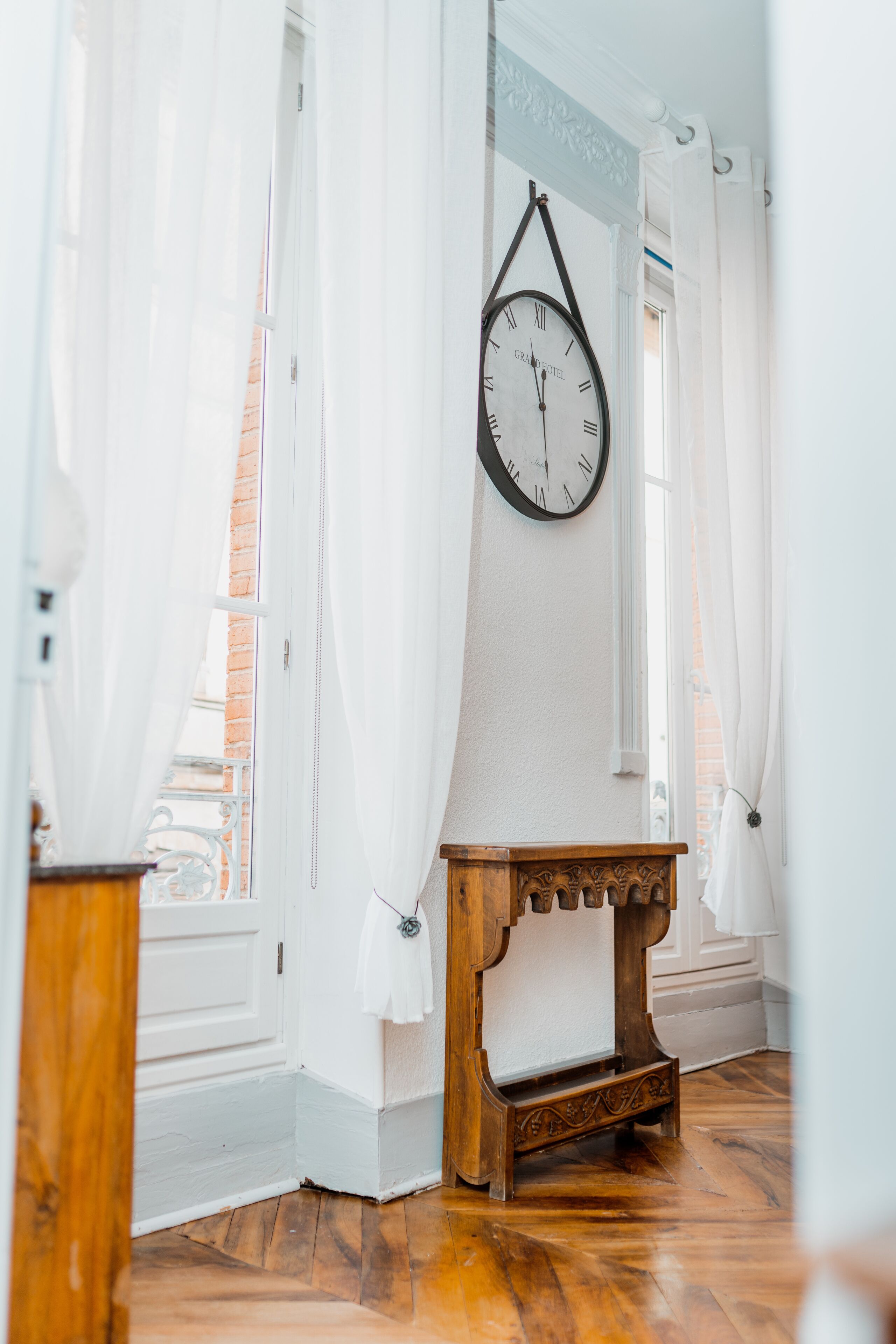 A room with a wooden bench, a wall-mounted clock, and white curtains.