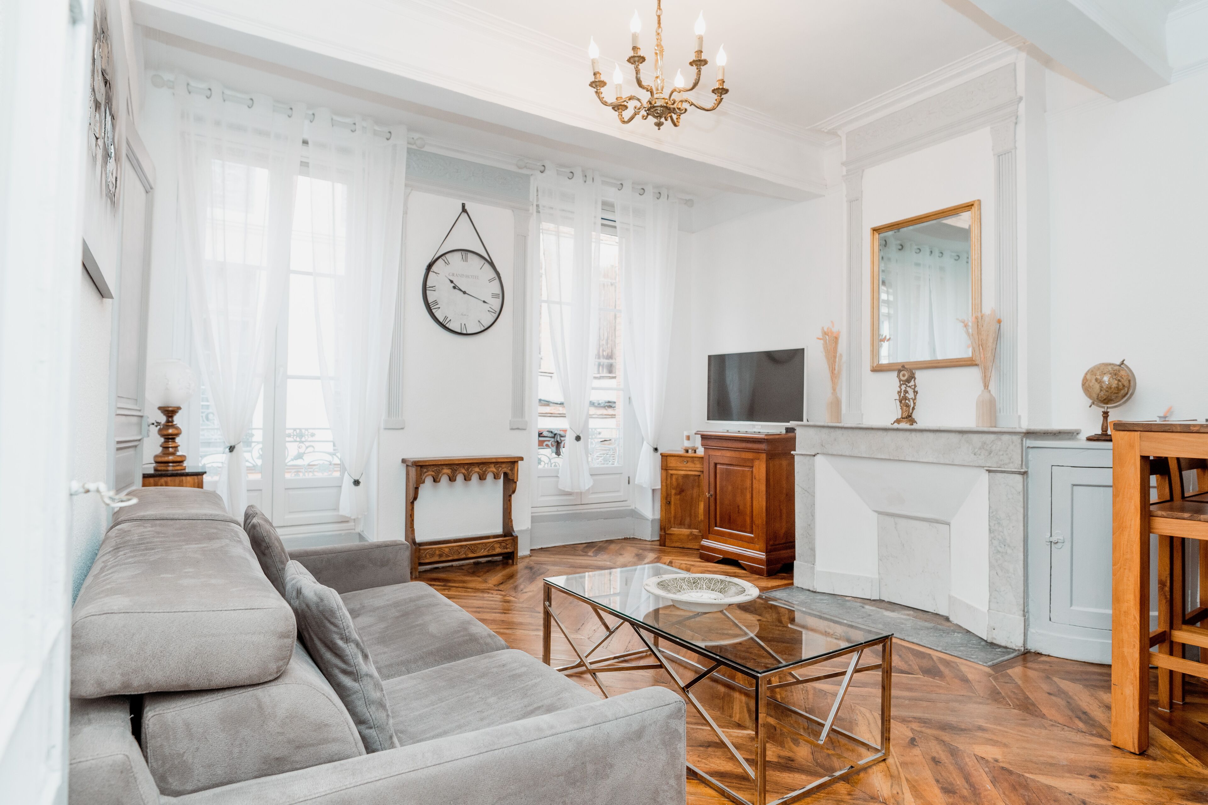 Un salon spacieux avec un canapé, une table basse en verre et un téléviseur. On y trouve également un meuble en bois et un miroir accroché au mur.