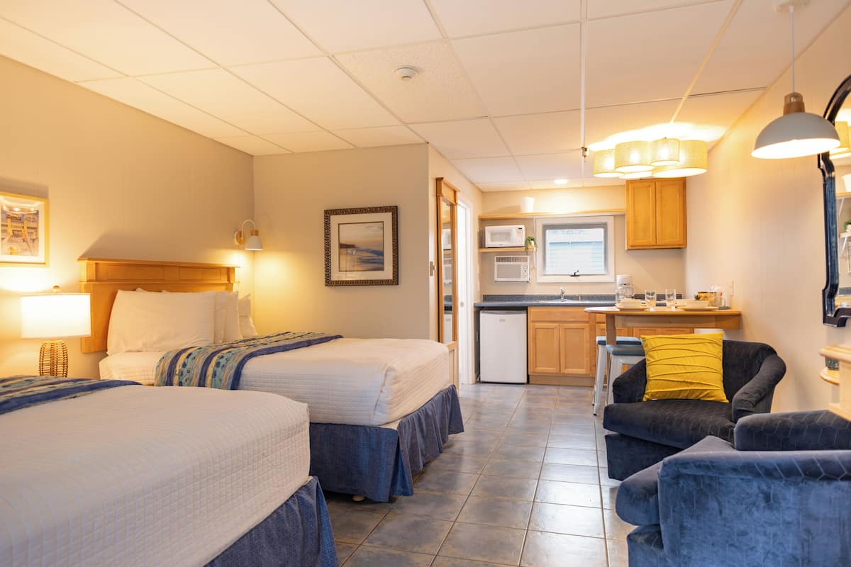 Hotelkamer met twee bedden, een kitchenette, een eethoek en een zithoek met een stoel en een tafel.