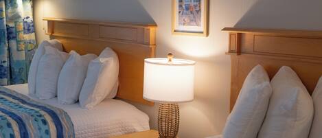 A hotel room with two beds, a bedside table with a lamp, a framed picture on the wall, and a curtain with a fish pattern.