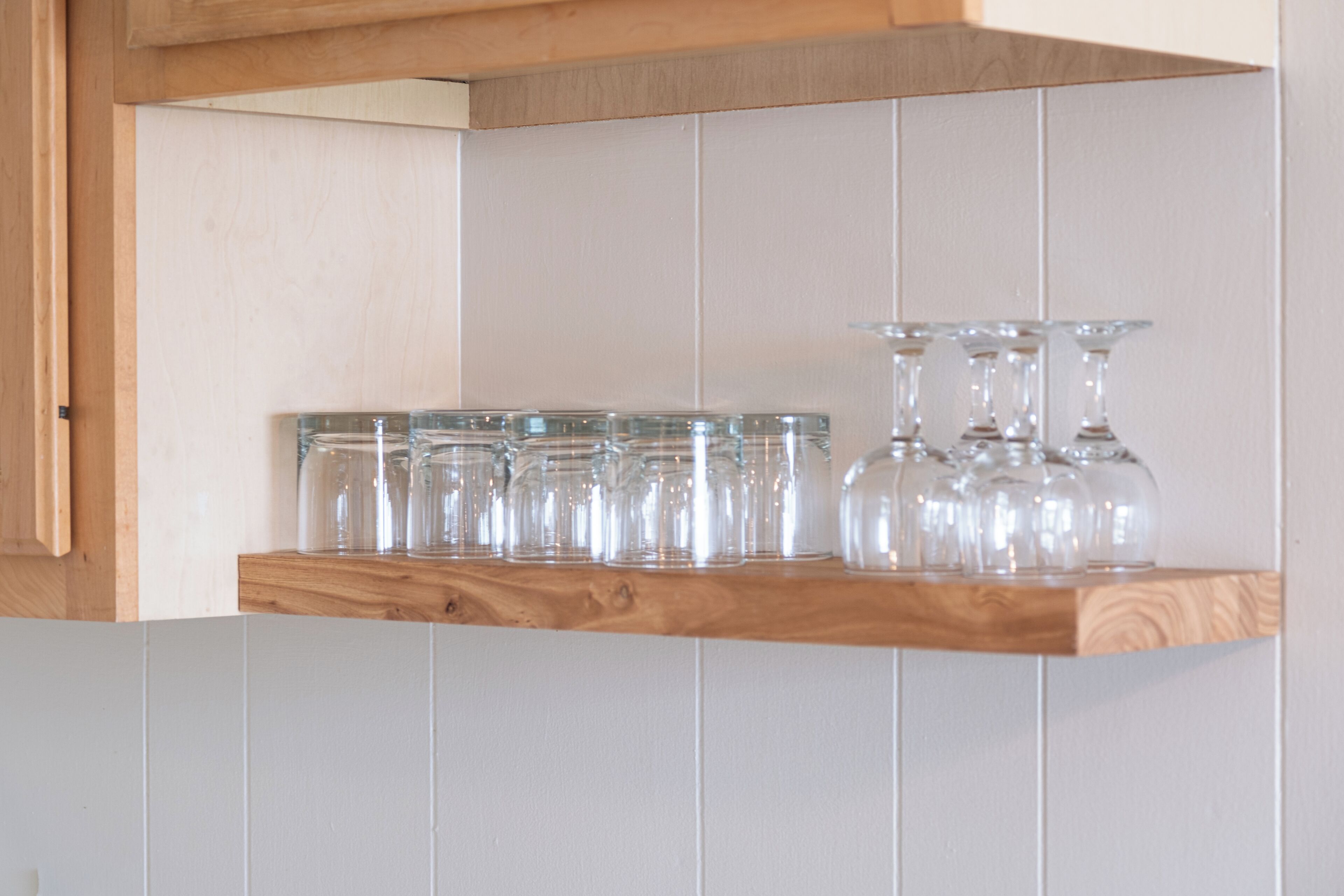 A kitchen shelf with glass jars and wine glasses.