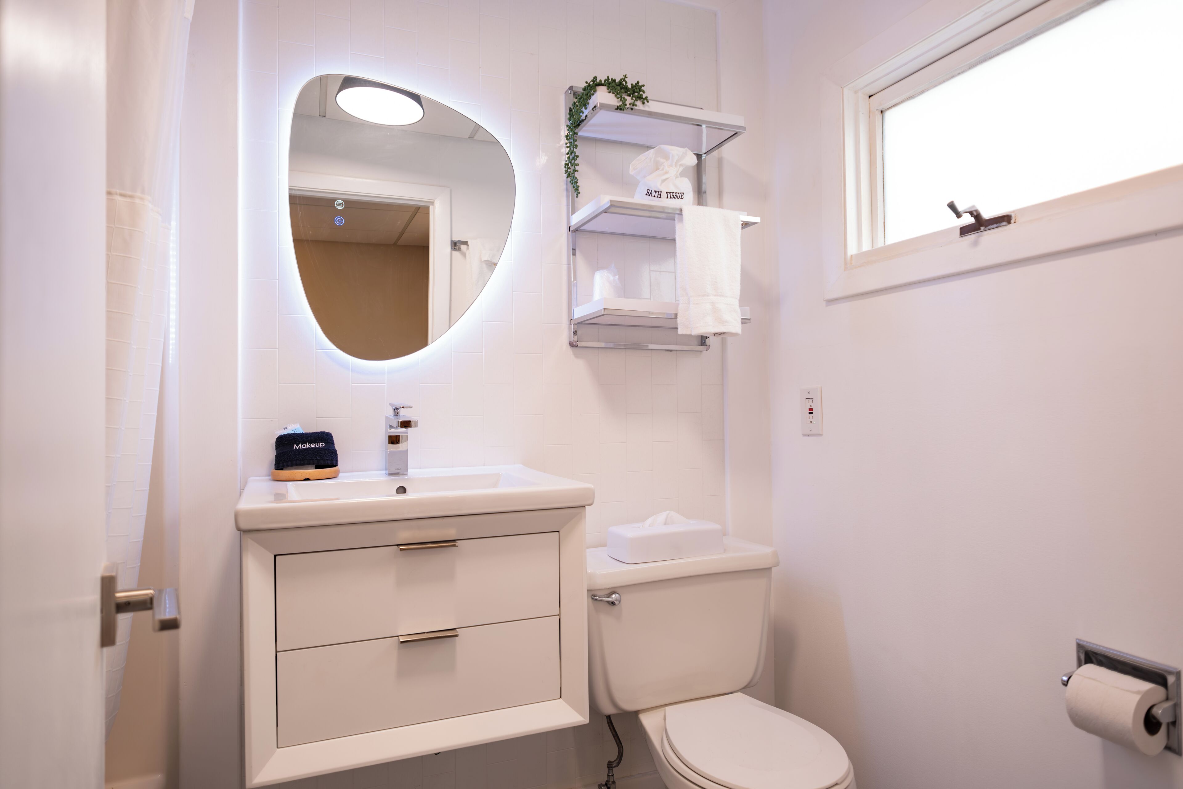 A bathroom with a white sink, a mirror, a toilet, and a window.