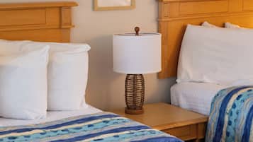 A hotel room with two beds, a bedside table with a lamp, and a framed picture on the wall.