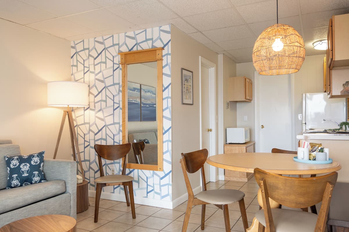 Een moderne woonkamer met een bank, stoelen, een eettafel en een keuken met een koelkast en magnetron.