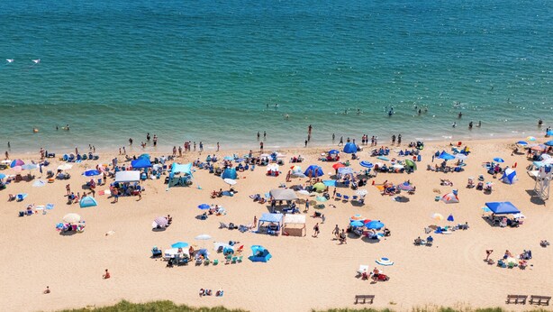 Une vue aĂ©rienne dâune plage oĂč lâon voit de nombreux parasols et des personnes.