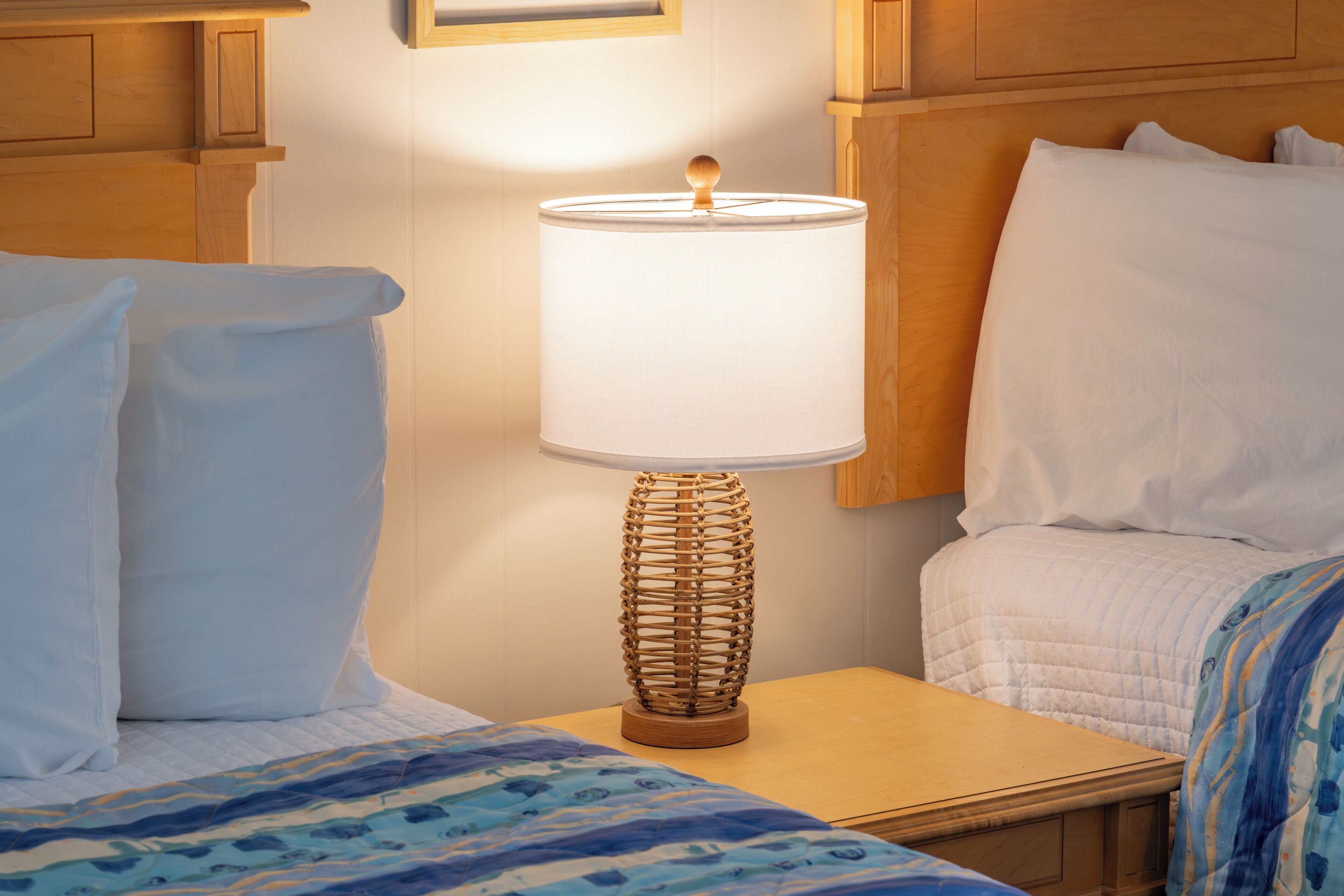 A hotel room with a wooden headboard, a bedside table with a lamp, and a bed with white bedding.