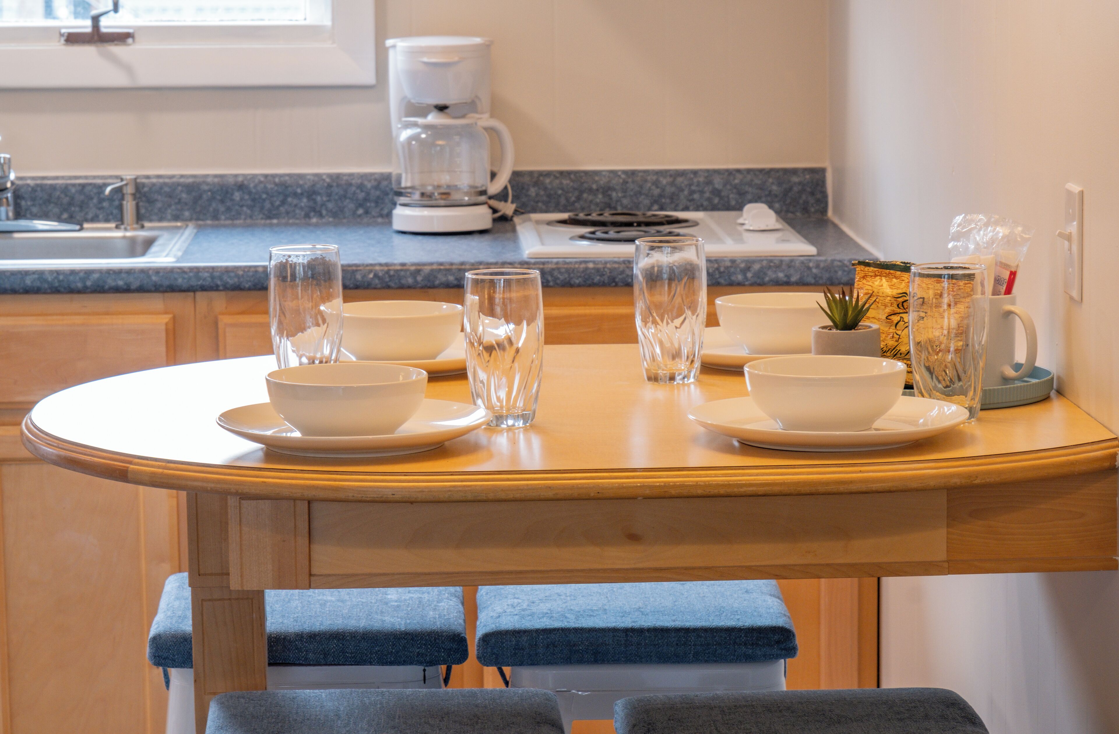 A kitchen with a dining table set for four, a coffee maker, and a sink.