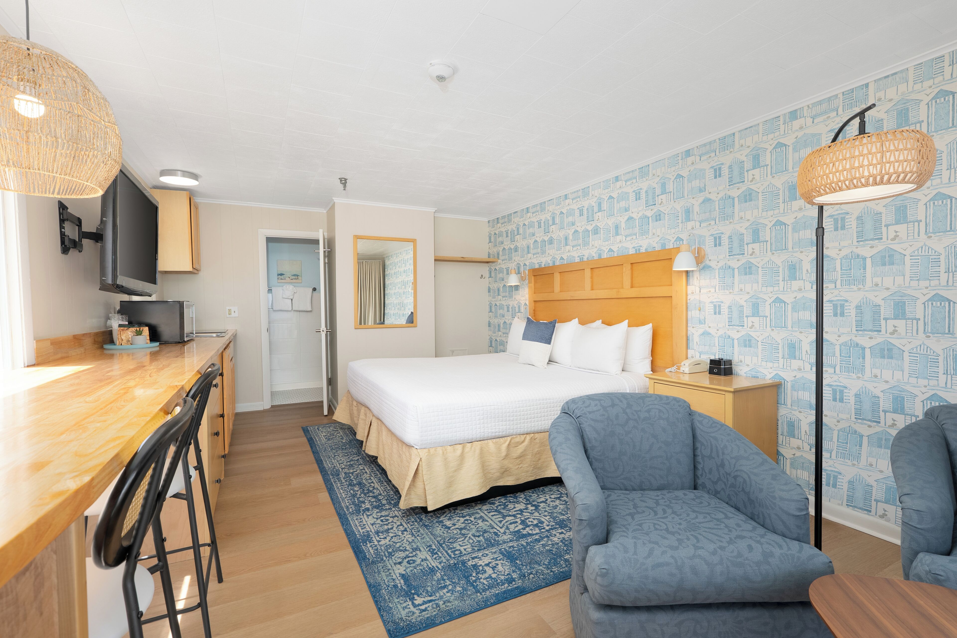 A hotel room with a bed, a desk with chairs, a television, and a patterned wall.