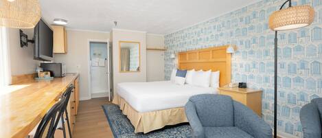 A hotel room with a bed, a desk with chairs, a television, and a patterned wall.