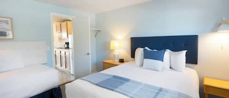 Habitación de hotel con dos camas, una kitchenette y un baño visible a través de una puerta abierta.