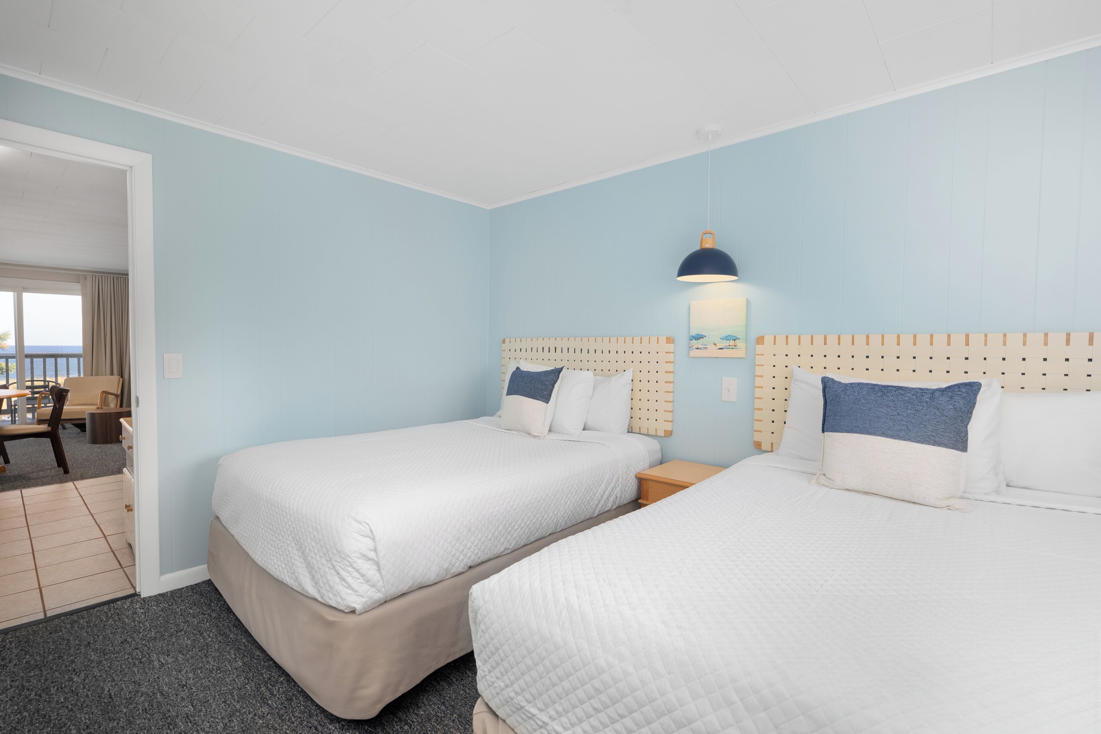Une chambre d’hôtel avec deux lits, une tête de lit en bois, une table de chevet, une lampe et une vue sur le balcon extérieur.