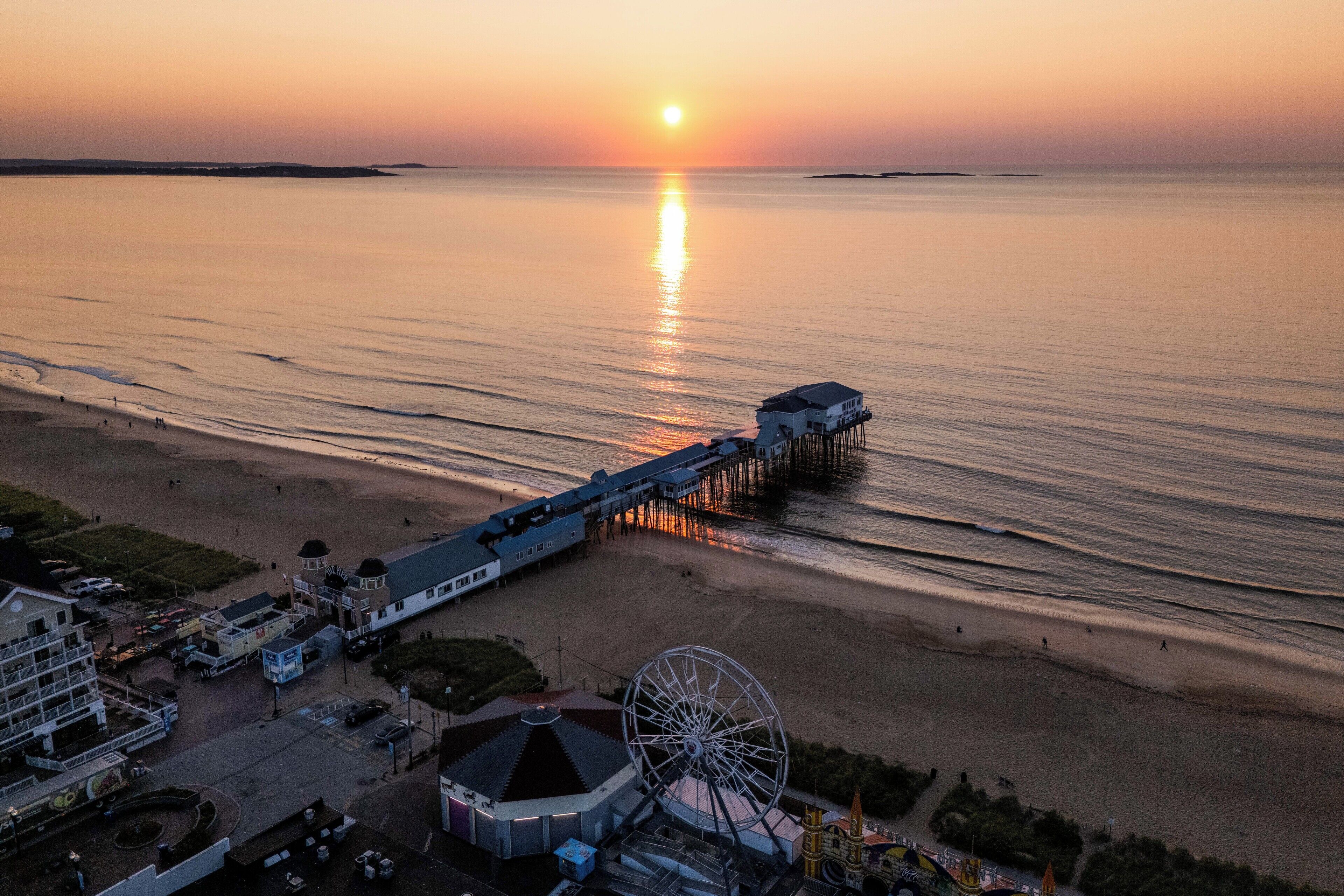 Eine Küstenlandschaft mit einer Promenade, die ins Meer ragt, einem großen Riesenrad und einem Gebäude mit einer Kuppel.