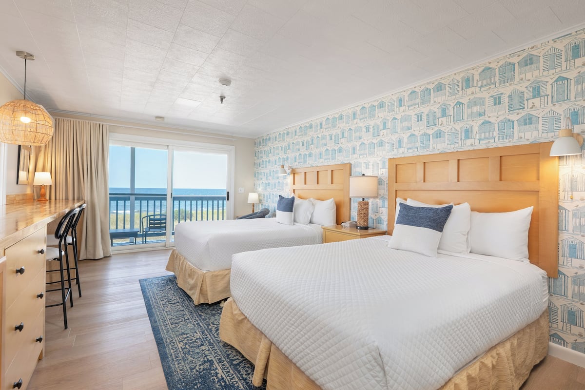 Een hotelkamer met twee bedden, een bureau en uitzicht op zee.