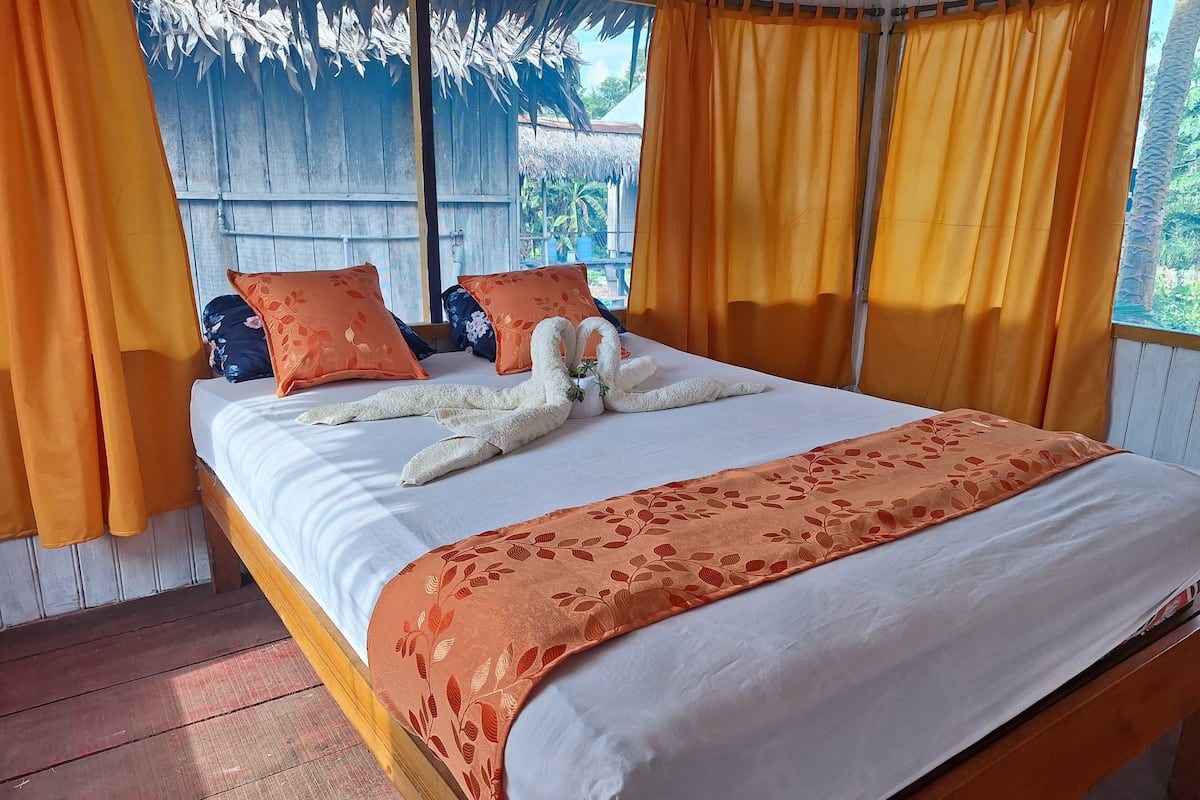 A bed with a white and orange floral bedspread, two orange pillows, and a decorative swan made of towels.