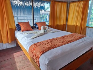 A bed with a white and orange floral bedspread, two orange pillows, and a decorative swan made of towels. - Canopy Tours Iquitos (Iquitos)