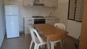 A compact kitchen with white cabinets, a gas stove, a sink, and a small refrigerator. - Angela Bungalow (Massa)