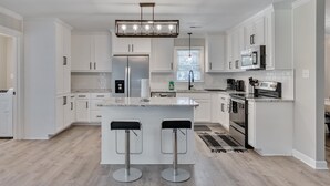 A modern kitchen with white cabinetry, a central island with bar stools, stainless steel appliances, and a pendant light.