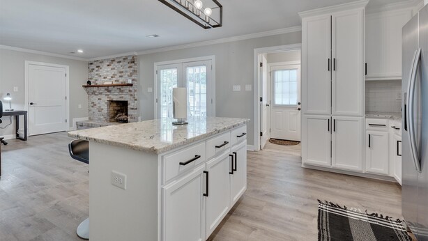A spacious kitchen with white cabinetry, a marble countertop island, and a built-in brick fireplace.