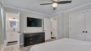 A bedroom with a bed, a dresser, a TV, and a ceiling fan.