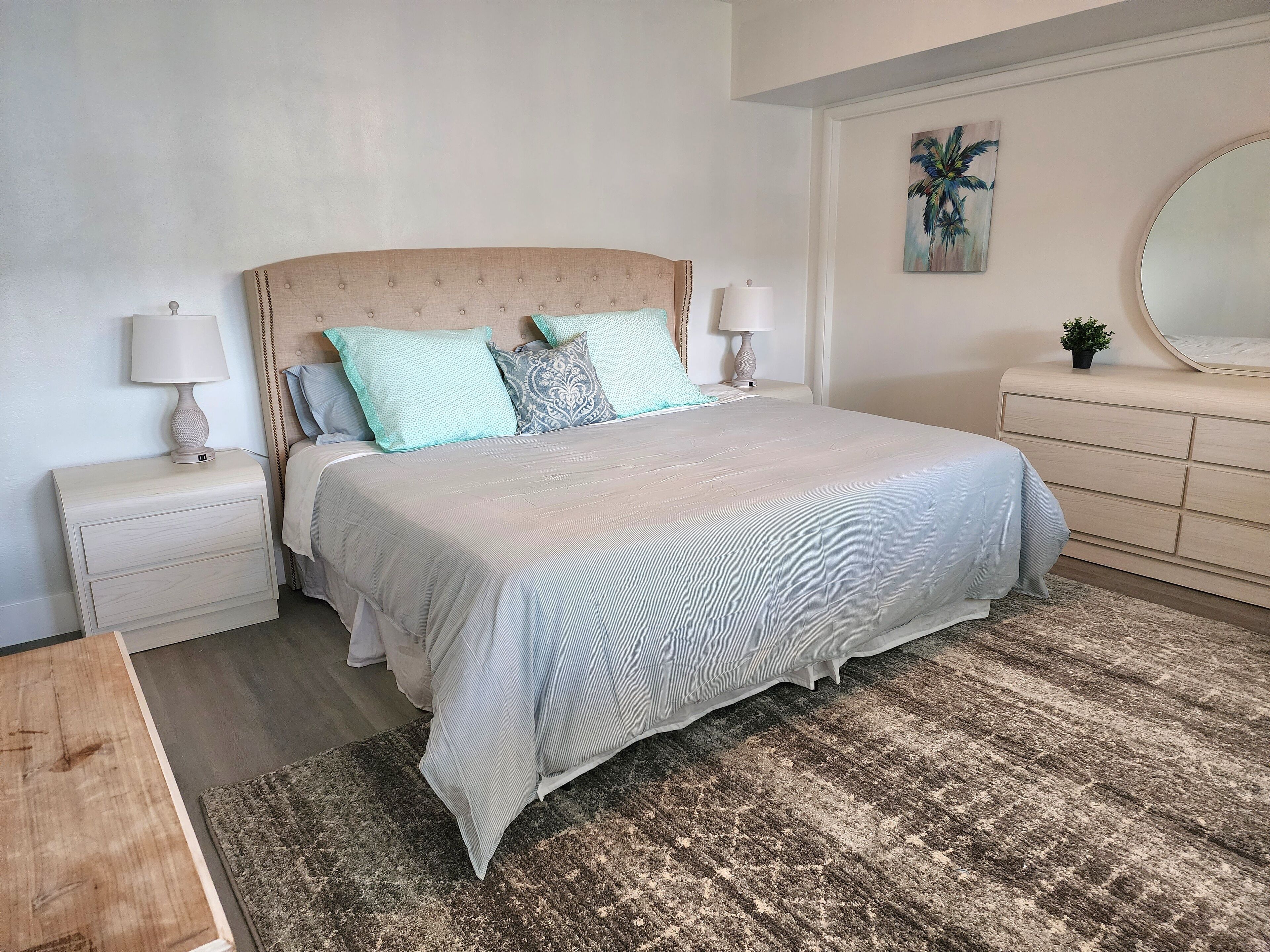 Une chambre à coucher avec un grand lit, deux tables de chevet, une commode, un miroir rond et un tableau mural.