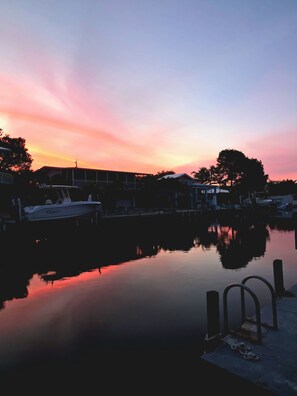Un puerto deportivo al atardecer, con aguas tranquilas que reflejan el cielo. Barcos amarrados y edificios al fondo.