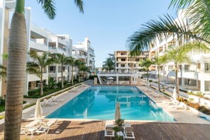A swimming pool surrounded by palm trees and white buildings with balconies.