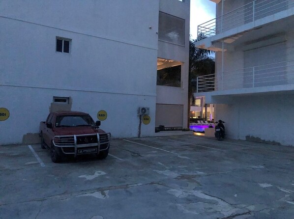 A parking area with a red pickup truck, a motorcycle, and a building with multiple floors and balconies.