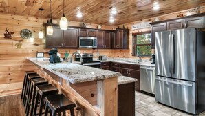 A wooden-paneled kitchen with a central island, stainless steel appliances, and bar stools.