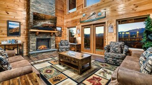 A cozy log cabin interior with a fireplace, leather sofas, and a stone fireplace surround.