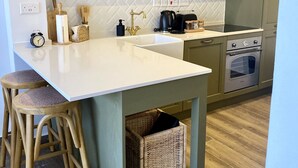 A kitchen with a white countertop, green cabinets, a built-in oven, and two wooden stools.