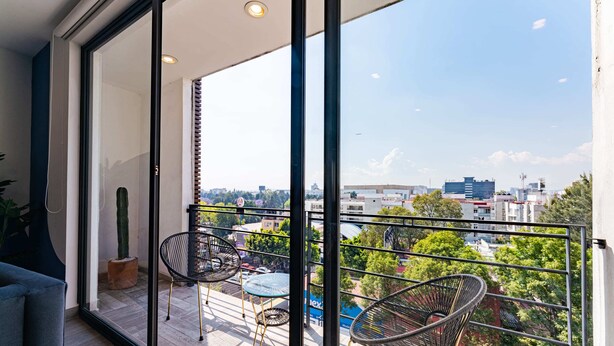 A balcony with a glass door, two wicker chairs, a small table, and a potted plant. - Roma Sur Apartments by VH (Mexico City)