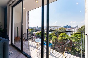A balcony with a glass door, two wicker chairs, a small table, and a potted plant. - Roma Sur Apartments by VH (Mexico City)