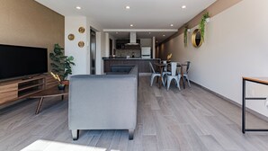 A modern living room with a flat-screen TV, grey sofa, and wooden entertainment unit. A dining area with a table and chairs is visible in the background. - Roma Sur Apartments by VH (Mexico City)