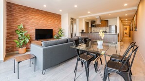 A modern living room with a grey sofa, a glass dining table, and black chairs. There is a TV mounted on the wall and a potted plant on the floor. - Roma Sur Apartments by VH (Mexico City)
