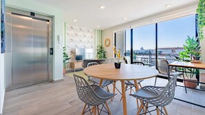 A modern dining area with a round table and chairs, a large window with a city view, and a wall-mounted TV. - Roma Sur Apartments by VH (Mexico City)