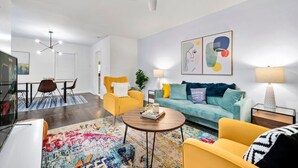 A modern living room with a sofa, armchairs, a coffee table, and a dining area with a table and chairs.