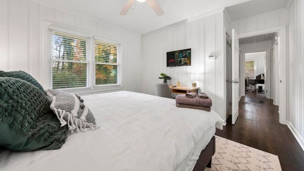 A bedroom with a bed, a desk, a chair, and a ceiling fan.