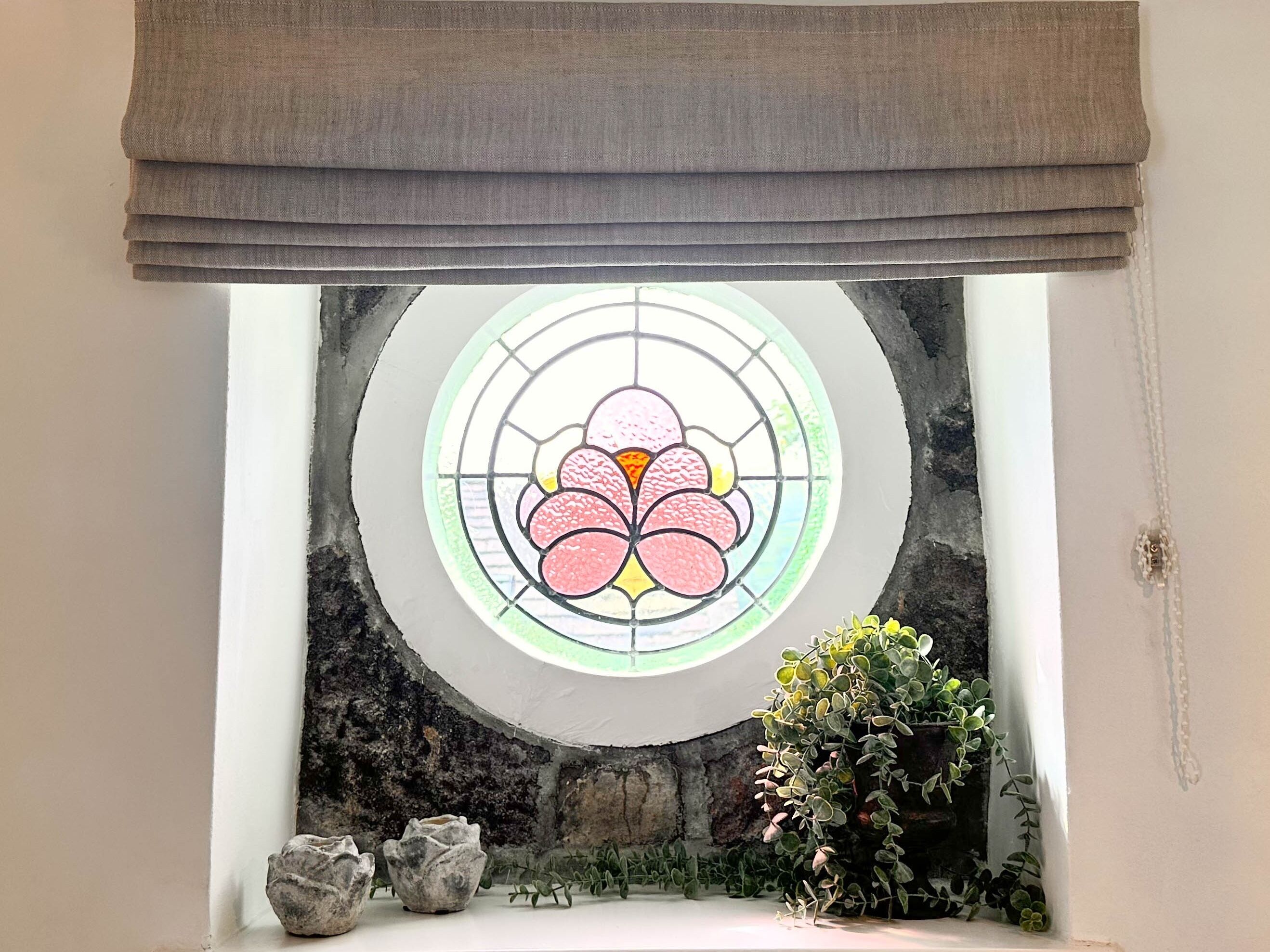 Una habitación con un amplio ventanal de vitral, pared de piedra y una planta en maceta.