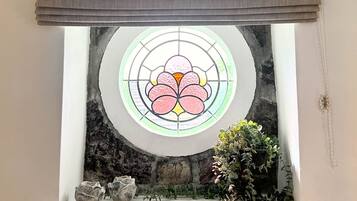 Una habitación con un amplio ventanal de vitral, pared de piedra y una planta en maceta.
