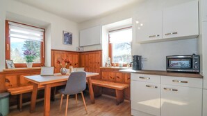 A compact kitchen with wooden cabinetry, a dining table, and a microwave. - Ferienwohnung in Irschen (Irschen)