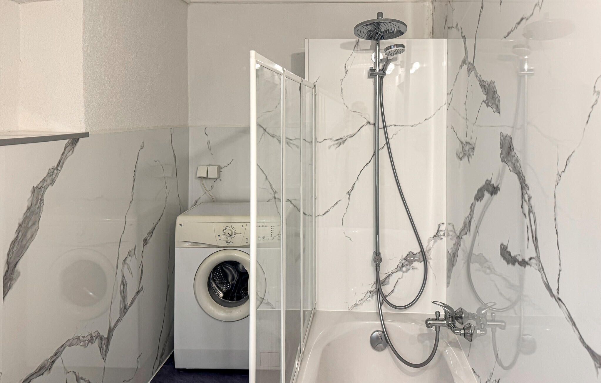 A bathroom with a shower, a washing machine, and marble-patterned walls.