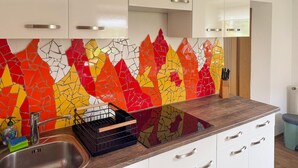 A kitchen with white cabinets, a colorful mosaic backsplash, a stainless steel sink, and a wooden countertop. - Ferienwohnung in Irschen (Irschen)