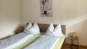 A double bed with patterned bedding, a wooden headboard, bedside tables with candles, and a wall-mounted picture. - Ferienwohnung in Irschen (Irschen)