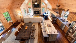 Ruime cabin-interieur met een eethoek, keuken en zithoek, met houten wanden en een stenen open haard.