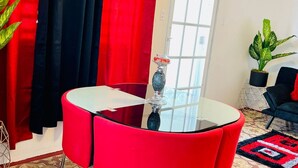 Ein modernes Wohnzimmer mit einem Couchtisch mit Glasplatte, roten und schwarzen Vorhängen, einer Topfpflanze und einem schwarzen Sofa.