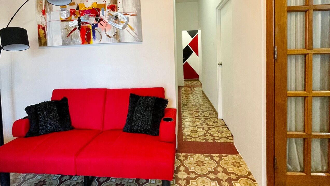 A red sofa with black cushions, a patterned carpet, and a wooden door with glass panels.